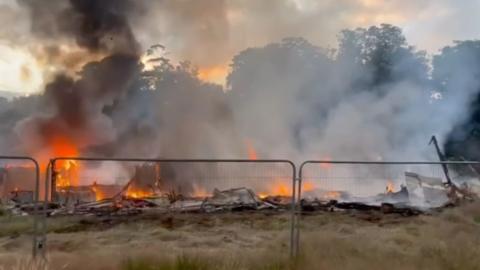 Flames and thick black smoke rise from fire site.