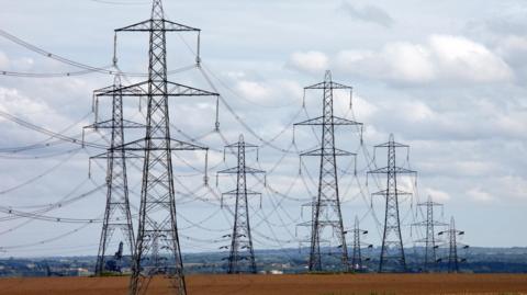 Electricity power transmission line pylons in abstract silhouette above ploughed agricultural fields