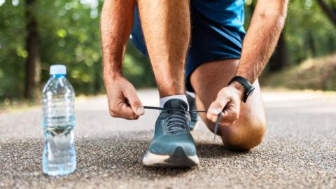 A man laces up his trainers with a water bottle beside him