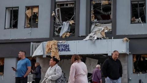 People stand at the site of a building housing the local branch of the British Council after it was hit by Russian missile and drone strikes. The multi storey building has had its windows blown out and suffered shrapnel and other severe structural damage.