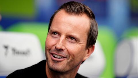 QPR manager Julien Stephan looks up and to the side smiling with teeth.