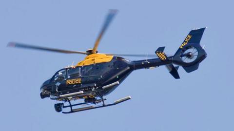 Strathclyde Police helicopter, Eurocopter EC135, rising from the Glasgow Heliport against a clear blue sky. The navy and yellow colours are used by all UK police forces. Personnel can be seen through the windows.