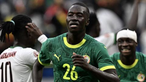 Pape Gueye, wearing a green Senegal shirt with the number 26 on the front, runs away in celebration
