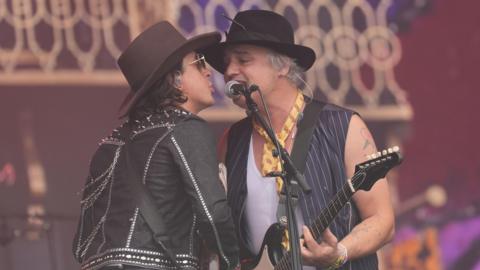Carl and Pete from The Libertines share a microphone as they perform on a festival stage. 