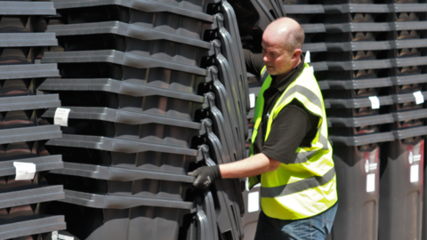 Man in hi vis jacket pushing a stack of black wheelie bins