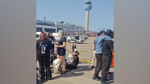 Passengers standing on the tarmac at East Midlands Airport. The air traffic control tower is in the background