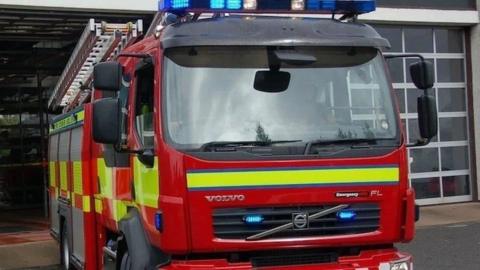 A red and yellow fire engine with its blue lights on exiting a fire station. 