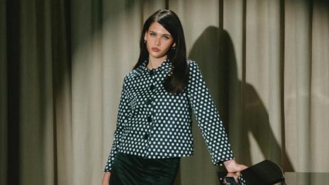 Sienna Spiro wears a black and white patterned jacket with black buttons. She has dark brown hair. 