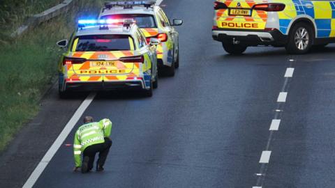 A police officer on a road alongside three police cars. 