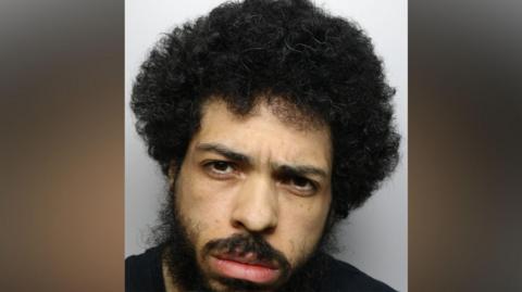 A police mugshot of Jason Spence, with curly black hair and a beard.