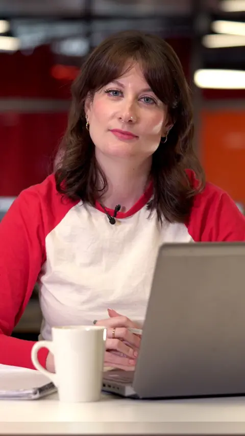 Gemma Dunstan in a red and white T shirt sat in front of a laptop and mug