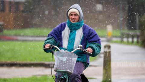 A woman wearing a rain jacket and a woolly hat riding a bicycle.