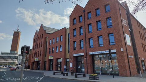 Three and four storey red brick buildings alongside a town centre road