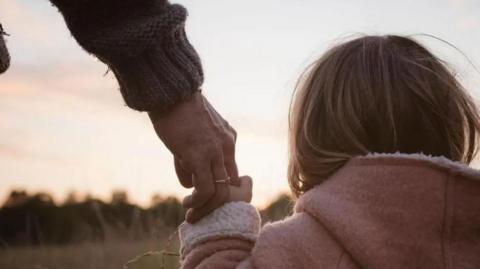 A young girl holding an adult's hand, looking over a field