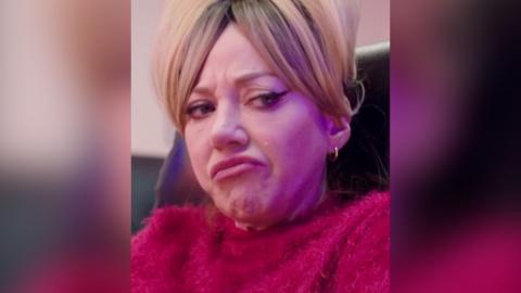 Mandy wearing a pink jumper and giving a side eye and a frown