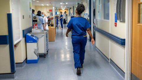 General view of hospital ward, with clinician in blue clothes walking down.