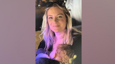 Charlotte Jelley is holding her baby daughter who is asleep in her arms. It is dark.