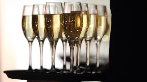 A tray of champagne flutes being carried by someone in silhouette. 