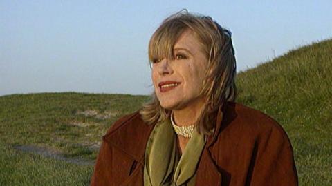 Marianne Faithfull smiling while sitting in a field