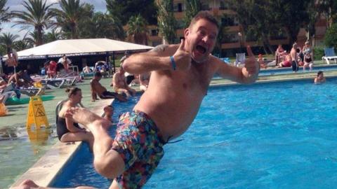 David Daly in swimming shorts jumping sideways into a outdoor swimming pool