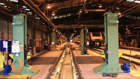 The inside of St Phillips Marsh train depot, with green beams, a stationary train. 