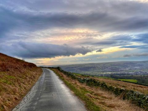 Grey sky over a country road on higher ground surrounded by fields 