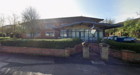 Google Maps image of the police station. There is a blue archway between stone pillars at the entrance and the building itself is red brick with several windows.