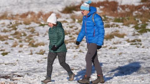 People walking in Bradgate Park in Leicestershire. They are wearing colourful green and blue puffer jackets and are wearing walking boots in the snow.