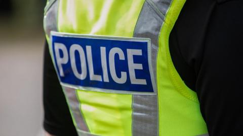 The back of a police officer's high-vis vest. It is yellow, with the word "Police" written across the back. 