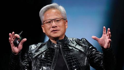 Nvidia's Jensen Huang, in his iconic black leather jacket, speaks on stage, gesturing with his hands up