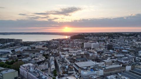 The sun sets over St Helier in this aerial photo. The bay is in the distance beyond which is a curved shoreline.
