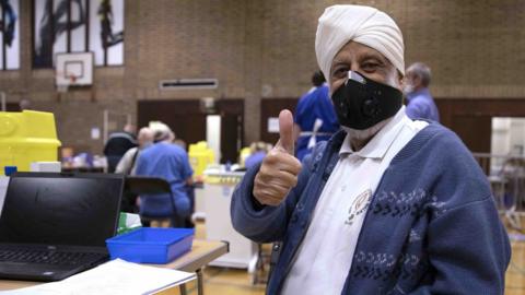 Sikh man gives a thumb-up after getting vaccinated in a sports centre