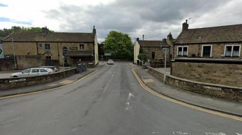 A Google Map photo of Bell Square in Silsden. It shows a road with two carriageways.