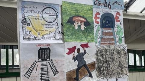 Amateur paintings and drawings which have been stuck to a banner, based on the events of the General Strike in the North East of England. Words and phrases adorn some of the artwork, such as "Coal or Dole" , "Left Behind for Money", and "Broken Lines". Most of the artwork depicts miners or railway immagery, in commemoration of the accidental derailing of a passenger train during the strike, which occured when striking miners sabotaged a local rail line to try and stop a coal train reaching its destination.