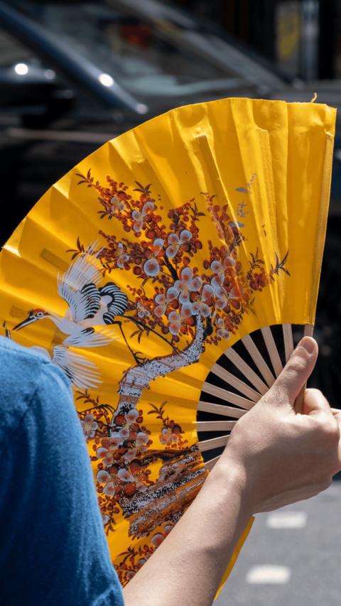 Close up of hand holding yellow fan with an ornate patterned design