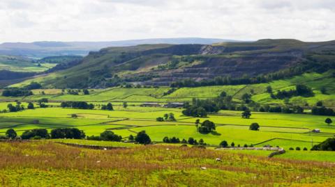 Image shows green rolling hills, trees with moorland in the background