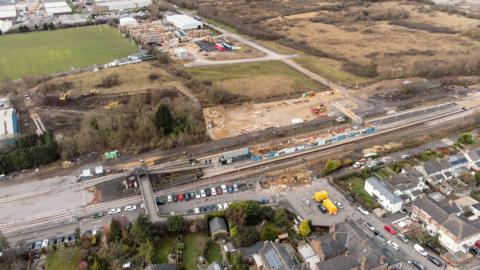 An aerial view of Eaglescliffe station. Cars can be seen parked outside of the station. Construction work can be seen taking place on the island platform. A large building site is present on the far side of the station.