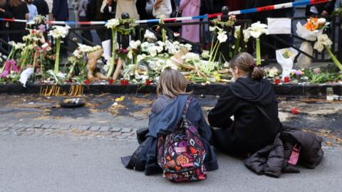 Girls sit on the pavement as people cue to sign the book of condolence for the victims of a shooting in front of the Vladislav Ribnikar elementary school in Belgrade, Serbia