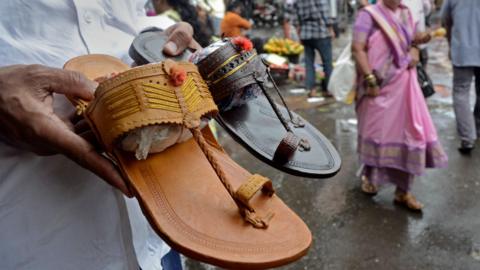 A shopkeeper holds Kolhapuri sandals, a traditional Indian style of footwear, at a roadside shop in Mumbai, India, on July 4, 2025. 