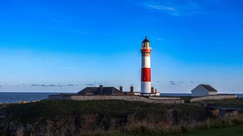 A red and white striped lighthouse stands out proudly against a deep blue sky and a crisp Scottish day