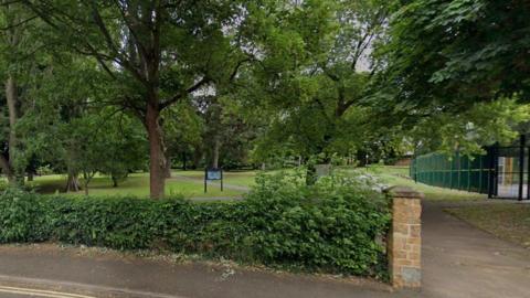 Hedging and path lead into the park with dense trees and lawn areas