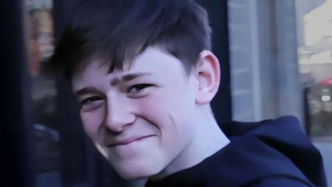 Ryan Morgan, with short dark hair and a dark hooded top, smiles at the camera