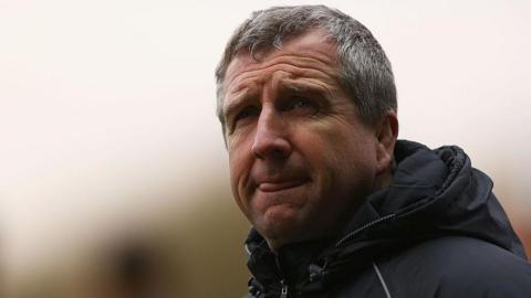 A grey haired man in a black coat, with a look of concentration staring off into the distance.