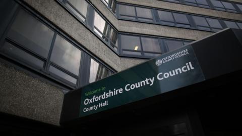 The sign on the building of Oxford County Hall, home of Oxfordshire County Council, photographed on a cloudy day