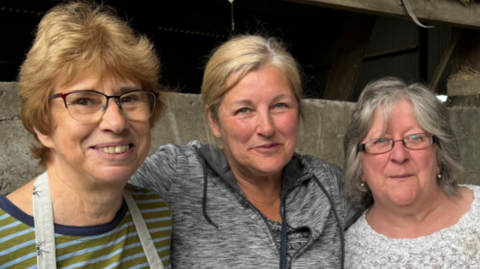 Three women standing with their arms around each other at a farm