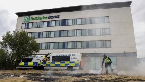 A police officer and two police vans outside the Holiday Inn Express in Manvers