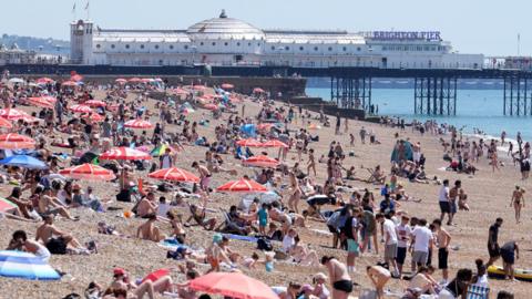 Lots of people sunbathing on a pebbled beach during a heatwave.