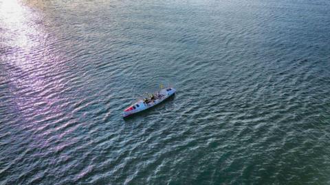 A drone image of a lone rowing boat in the middle of the ocean.