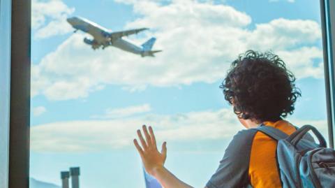 A boy looks up at a plane through a window