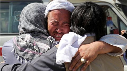 Afghan men hug each other as they mourn during the funeral of their relatives after a wedding suicide bomb blast in Kabul